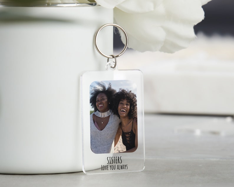 May include: A clear acrylic keychain with a photo of two women smiling. The keychain has the text "Sisters Love You Always" printed on the bottom.