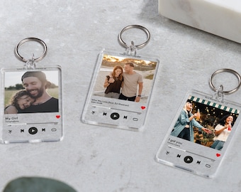 May include: Three clear acrylic keychains with photos and song titles. The keychains feature a play button, a heart icon, and a progress bar. The first keychain has a photo of a father and daughter with the song title "My Girl" by The Temptations. The second keychain has a photo of a couple with the song title "When My Love Feels Like Ed Sheeran" by Sam Smith. The third keychain has a photo of two friends with the song title "I got you" by  Leona Lewis.