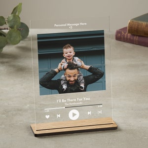 May include: A clear acrylic photo frame with a wood base. The frame features a photo of a father and son, with the son sitting on the father's shoulders. The frame also includes a music player design with the song title "I'll Be There For You" by The Rembrandts.