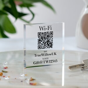 以下が含まれることがあります： 白地に黒と白のQRコード、テキスト「Wi-Fi」、「NAME: TrueWillowUK」、「PASSWORD: Gift@TW12345」が書かれた透明なアクリルブロックです。