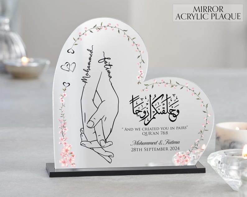 May include: A heart-shaped mirror acrylic plaque with a floral design and the names "Mohammed" and "Fatima" written in cursive. The plaque also features a quote from the Quran: "And We created you in pairs." The date "28th September 2024" is written below the quote.