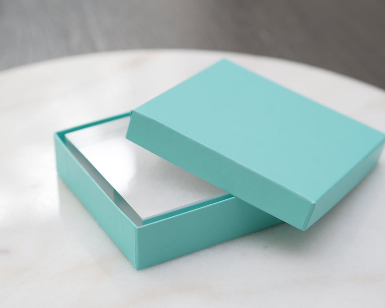 May include: A light blue gift box with a white interior. The lid is open and the box is sitting on a white surface.