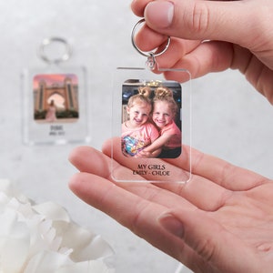 May include: A clear acrylic keychain with a photo of two young girls smiling. The text "MY GIRLS EMILY - CHLOE" is printed below the photo.