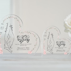 May include: Two clear acrylic heart-shaped plaques with floral designs and the names "Mohammed" and "Fatima" inscribed. The text "And we created you in pairs" is also included, along with a Quran verse reference and a wedding date.