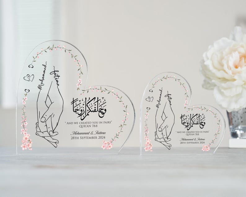 May include: Two clear acrylic heart-shaped plaques with floral designs and the names "Mohammed" and "Fatima" inscribed. The text "And we created you in pairs" is also included, along with a Quran verse reference and a wedding date.
