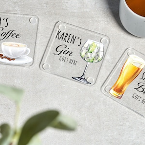 May include: Three clear glass coasters with personalized text and images. The first coaster says "Mum's Coffee Goes Here" and features a cup of coffee. The second coaster says "Karen's Gin Goes Here" and features a glass of gin with lime. The third coaster says "Sanjay's Beer Goes Here" and features a glass of beer.