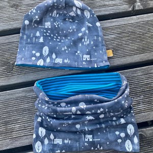 Peut inclure: Ensemble assorti bonnet et tour de cou. Le bonnet est de style bonnet avec une bordure bleue. Le tour de cou est une écharpe tubulaire. Les deux articles sont bleu foncé avec un motif de forêt et de maison blanc. L'intérieur du tour de cou est à rayures bleues et blanches.