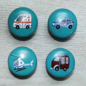 Könnte beinhalten: Vier tealblaue runde Holzknöpfe mit gemalten Bildern eines Krankenwagens, eines Polizeiautos, eines Hubschraubers und eines Feuerwehrautos. Der Krankenwagen hat ein rotes Kreuz an der Seite. Das Polizeiauto hat das Wort "Polizei" an der Seite. Das Feuerwehrauto hat eine Leiter an der Seite.
