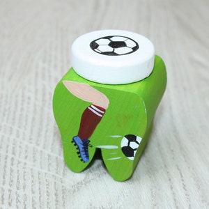 May include: Green wooden tooth-shaped box with a soccer player kicking a ball on the front. The lid is white with a black and white soccer ball on top.