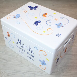 May include: White wooden storage box with a blue, orange, and yellow butterfly design. The box is decorated with the name "Moritz" and the date "15.04.2020 23:45 46.15cm 3950g".