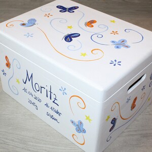 May include: White wooden keepsake box with a blue and orange butterfly design. The box is personalized with the name "Moritz" and the date "15.04.2020".