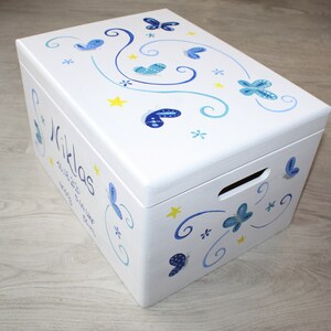 May include: White wooden box with a blue and yellow butterfly design. The box is personalized with the name "Niklas" and the date "Nov 18, 2022".