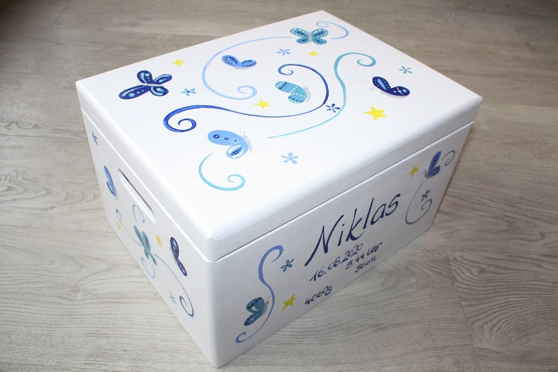 May include: White wooden keepsake box with a blue and yellow butterfly design. The box is personalized with the name "Niklas" and the date "16.08.2020".