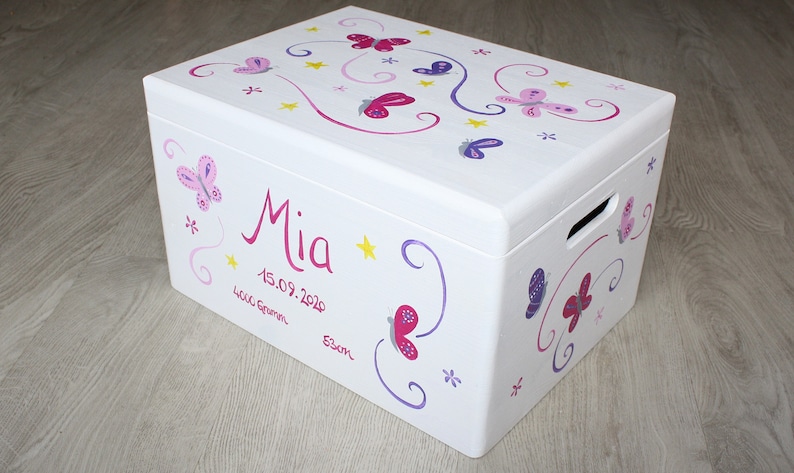 May include: White wooden storage box with a butterfly and star design. The box is painted with pink, purple, and yellow butterflies and stars. The name "Mia" is written in pink lettering on the front of the box, along with the date "15.09.2020".