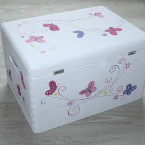 May include: White wooden storage chest with a butterfly design. The chest is decorated with pink, purple, and red butterflies on a white background.