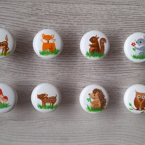 Könnte beinhalten: Acht Holz-Knöpfe mit bemalten Waldtier-Motiven. Die Knöpfe zeigen ein Reh, einen Fuchs, ein Eichhörnchen, eine Maus, einen Pilz, ein Wildschwein, einen Igel und eine Eule.