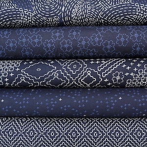 Op de afbeelding: Vijf rollen donkerblauwe stof met witte stiksels in verschillende geometrische patronen. De stof is een traditionele Japanse sashiko-stijl.