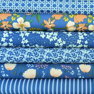 Könnte beinhalten: Ein Stapel blauer Stoffrollen mit verschiedenen floralen und geometrischen Mustern. Die Stoffe zeigen Designs mit weißen Blumen, pfirsichfarbenen Blüten und blauen Blättern. Ein Stoff hat ein Streifenmuster. Maße in Zentimetern.