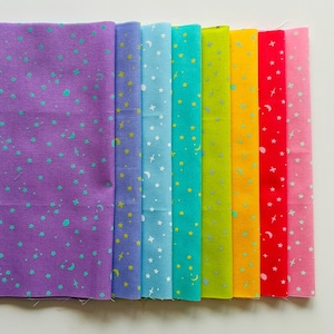 Könnte beinhalten: Eine Sammlung von acht Stoffmustern in verschiedenen Farben, jedes mit einem Himmelsmuster aus Sternen und Monden verziert. Die Farben umfassen Lila, Blau, Türkis, Grün, Gelb, Rot und Rosa. Der Stoff ist wahrscheinlich Baumwolle.