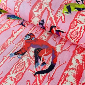 Könnte beinhalten: Rosa Stoff mit einem sich wiederholenden Muster aus roten Bäumen, Affen und Vögeln. Die Affen sind rot mit lila Akzenten und blauen Händen und Füßen. Die Vögel sind grün, blau und gelb. Der Stoff hat ein Streifendesign.