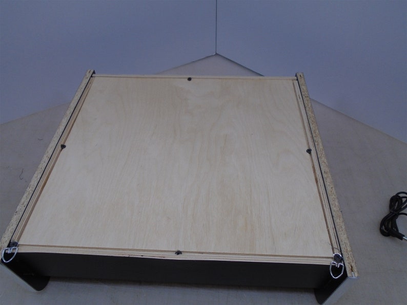 May include: The back of a wooden picture frame with a light wood finish. The frame has a black border and two metal hanging hooks.