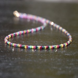 Pu&ograve; includere: Una delicata collana composta da piccole pietre preziose colorate. La collana presenta una variet&agrave; di colori, tra cui rosso, giallo, verde e blu, infilati insieme. La chiusura sembra essere dorata. Le pietre preziose sono uniformemente distanziate.