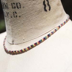 Pu&ograve; includere: Una delicata collana composta da piccole pietre preziose colorate. Le perline sono disposte in un motivo arcobaleno, con sfumature di rosso, giallo, verde, blu e viola. La collana &egrave; esposta su un manichino, mettendo in risalto i suoi colori vivaci e il design.