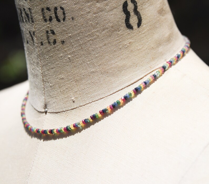 Pu&ograve; includere: Una delicata collana composta da piccole pietre preziose colorate. Le perline sono disposte in un motivo arcobaleno, con sfumature di rosso, giallo, verde, blu e viola. La collana &egrave; esposta su un manichino, mettendo in risalto i suoi colori vivaci e il design.