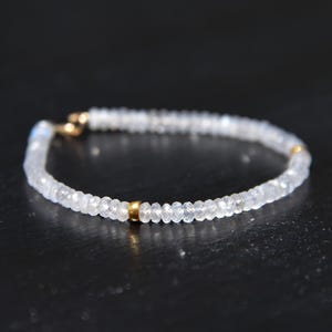 May include: Delicate bracelet featuring small, faceted, clear beads strung together. The bracelet has gold-colored accents at the clasp and center. The jewelry is designed to be worn around the wrist.