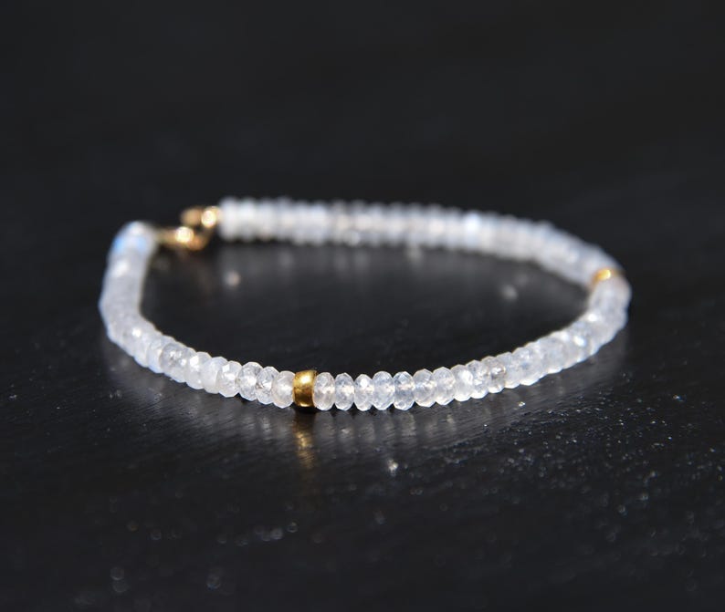 May include: Delicate bracelet featuring small, faceted, clear beads strung together. The bracelet has gold-colored accents at the clasp and center. The jewelry is designed to be worn around the wrist.