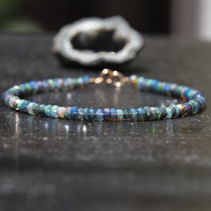 May include: A delicate bracelet made with small, iridescent black opal beads. The bracelet is strung on a thin gold chain and has a simple clasp.