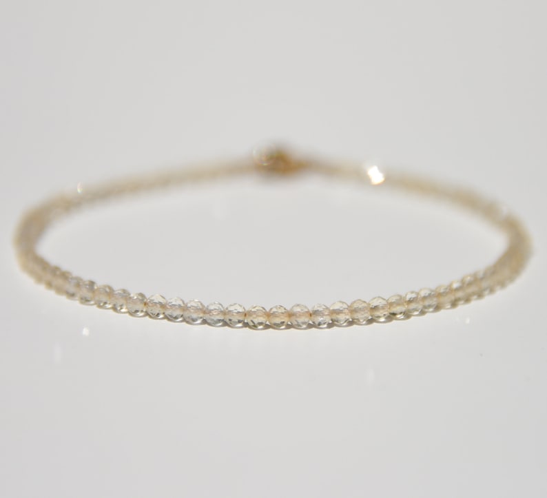K&ouml;nnte beinhalten: Ein zartes Armband aus kleinen, klaren Perlen mit einem goldenen Verschluss.
