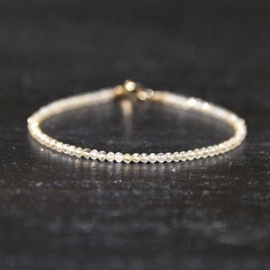K&ouml;nnte beinhalten: Ein zartes Armband aus kleinen, klaren Perlen mit einem goldenen Verschluss.