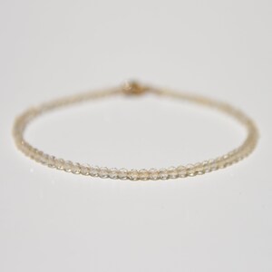 K&ouml;nnte beinhalten: Ein zartes Armband aus kleinen, klaren Quarzperlen, die auf einer d&uuml;nnen goldenen Kette aufgef&auml;delt sind.