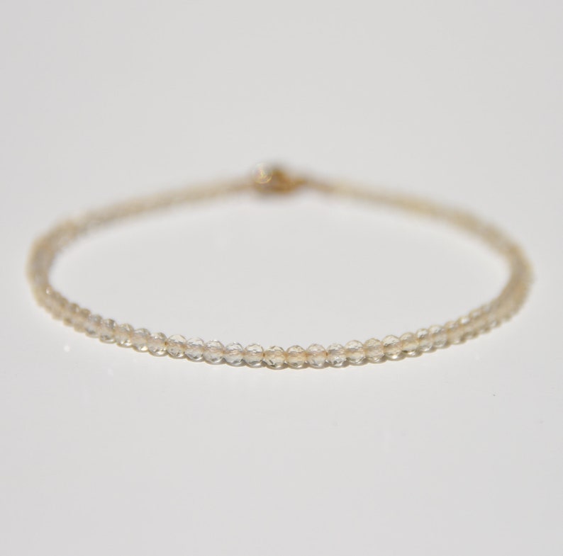 K&ouml;nnte beinhalten: Ein zartes Armband aus kleinen, klaren Quarzperlen, die auf einer d&uuml;nnen goldenen Kette aufgef&auml;delt sind.