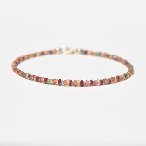 May include: A delicate bracelet made of small, colourful gemstones. The bracelet features a variety of colours, including red, yellow, green, and orange, strung together with a silver clasp. The gemstones are small and evenly spaced.