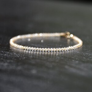 K&ouml;nnte beinhalten: Ein zartes Armband aus kleinen, klaren Perlen mit einem goldenen Verschluss.