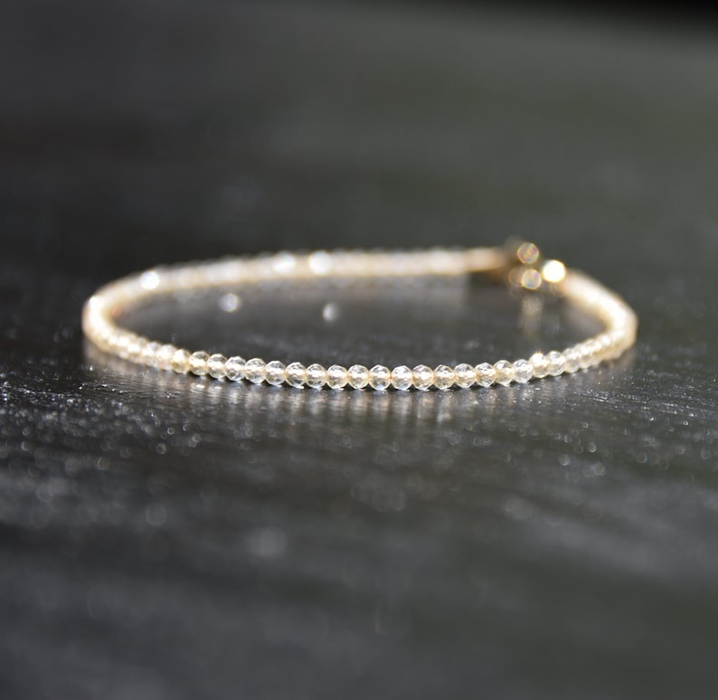 K&ouml;nnte beinhalten: Ein zartes Armband aus kleinen, klaren Perlen mit einem goldenen Verschluss.