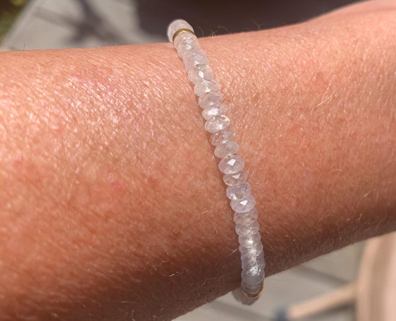 May include: A delicate bracelet featuring small, faceted, clear beads strung together. The bracelet is accented with gold-colored metal elements. The beads appear to be made of a translucent material, reflecting light.