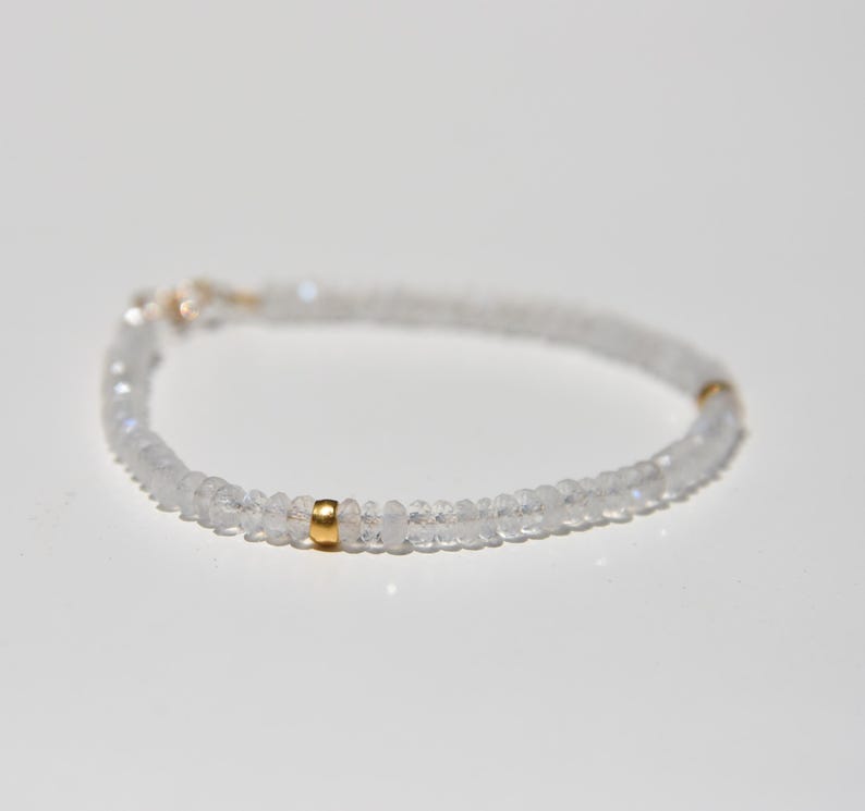 May include: Delicate bracelet featuring small, clear, round beads. The bracelet has a gold-colored clasp and a gold-colored accent bead. The beads are strung together to form a flexible band, creating a minimalist and elegant design.