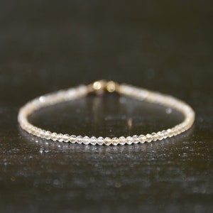 K&ouml;nnte beinhalten: Ein zartes Armband aus kleinen, klaren Perlen. Das Armband hat einen goldenen Verschluss.