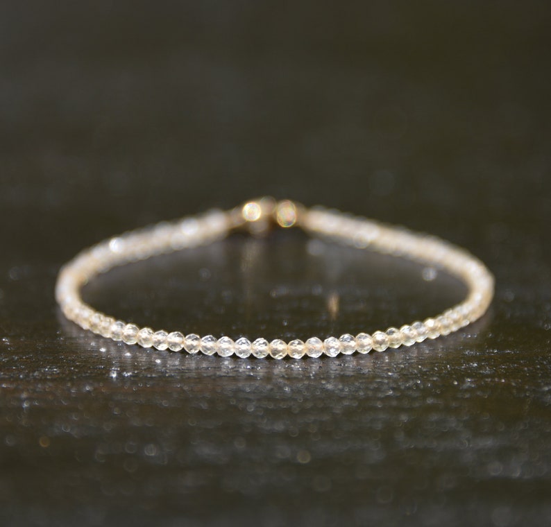 K&ouml;nnte beinhalten: Ein zartes Armband aus kleinen, klaren Perlen. Das Armband hat einen goldenen Verschluss.