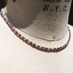 Pu&ograve; includere: Una collana di perline colorate con una variet&agrave; di piccole pietre preziose rotonde. La collana presenta uno spettro di colori, tra cui rosso, blu, verde e giallo. La collana &egrave; esposta su un manichino.