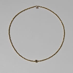 May include: A delicate gold necklace featuring a fine chain of small, round beads. The necklace has a simple design with a single, slightly larger bead near the center and a clasp closure. The jewelry is displayed against a plain white background.