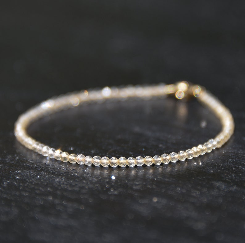 K&ouml;nnte beinhalten: Ein zartes Armband aus kleinen, klaren Perlen mit einem goldenen Verschluss.