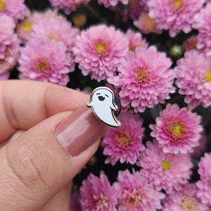 Peut inclure: Une épingle en émail blanc avec un motif de fantôme souriant. L'épingle est dorée et a un dos en caoutchouc noir.