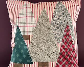 May include: A decorative pillow featuring a patchwork design of Christmas trees. The trees are made from various fabrics, including plaid, polka dots, and floral patterns. The pillow has a red and white striped background.