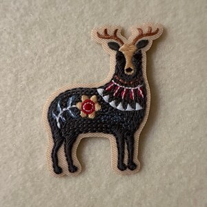 Pode incluir: Patch de veado preto bordado com uma flor vermelha e azul, contas brancas e vermelhas e chifres marrons.