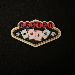 Op de afbeelding: Witte en gouden geborduurde patch met het woord "CASINO" in rode letters en vier speelkaarten in het midden. De patch heeft de vorm van een ruit.