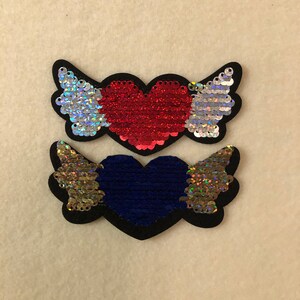 Puede incluir: Dos parches para planchar con corazones y alas de lentejuelas. El parche superior tiene un corazón rojo con alas blancas y plateadas. El parche inferior tiene un corazón azul con alas doradas.